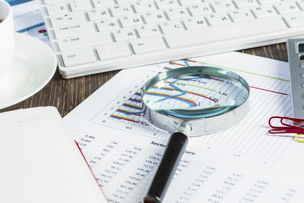 Magnifing glass and documents with analytics data lying on table Magnifing glass and documents with analytics data lying on table